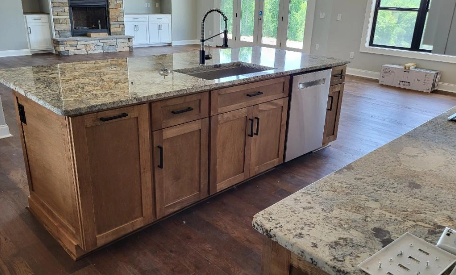 A kitchen island with a light granite countertop, dark wood cabinets, a sink, and a dishwasher in a home.